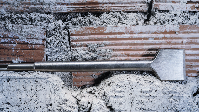 Flat chisel positioned against a brick wall with cement debris.