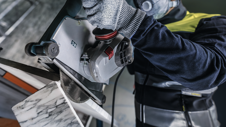 A person wearing safety equipment cuts a marble slab with a circular saw.