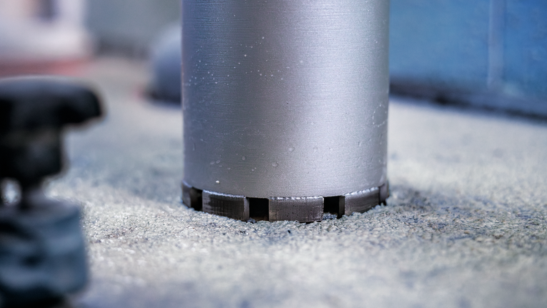 A core drill bit makes a circular cut in concrete flooring.