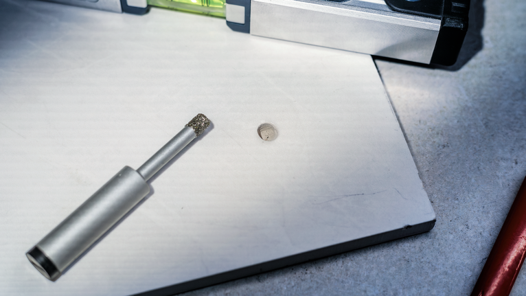 Diamond drill bit and level tool on a white tile with a freshly drilled hole.