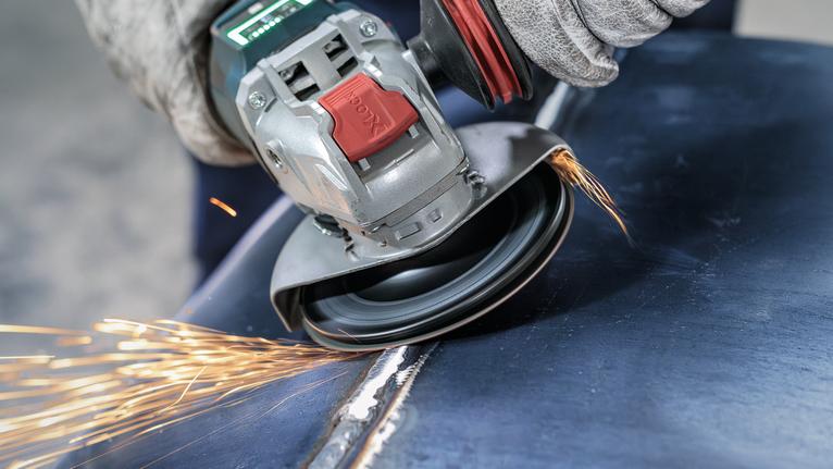 Person wearing safety equipment grinds a metal surface with an angle grinder.