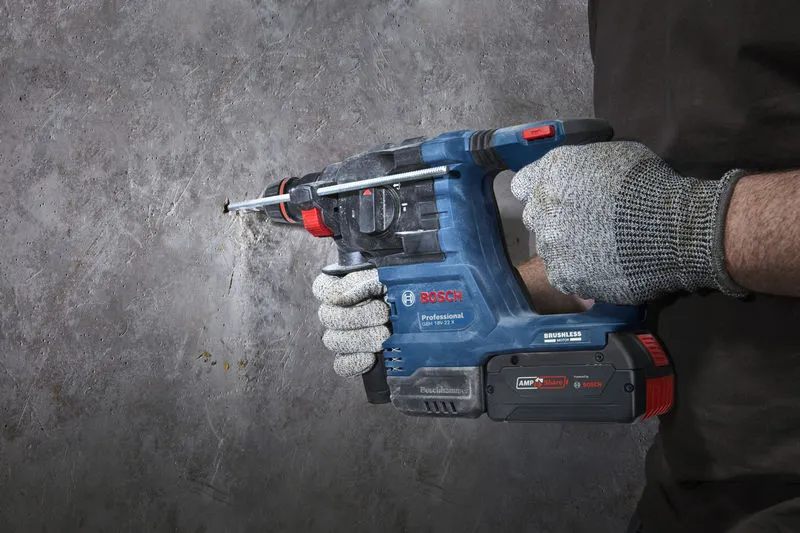 A person wearing safety equipment drills into a concrete wall using a rotary hammer.