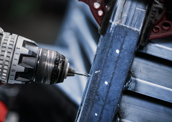 Power drill creating a hole in a blue metal beam.