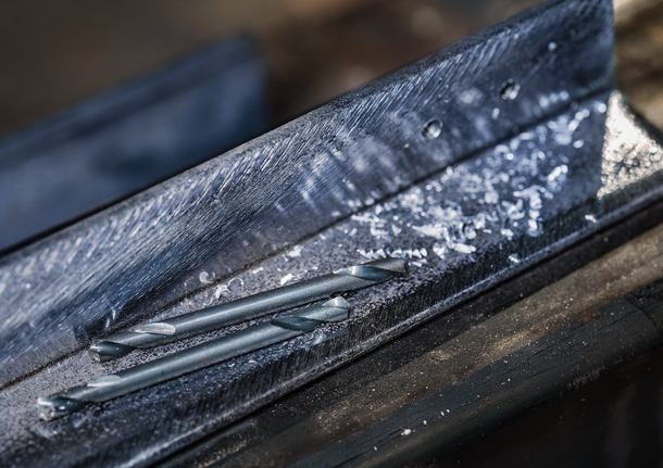 Drill bits lying on a metal beam with metal shavings scattered around.