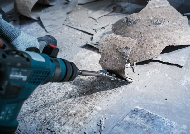 Person wearing safety equipment removes old flooring with a power chisel.