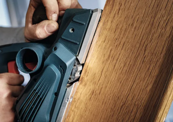 Person uses a power planer to smooth the edge of a wooden board.