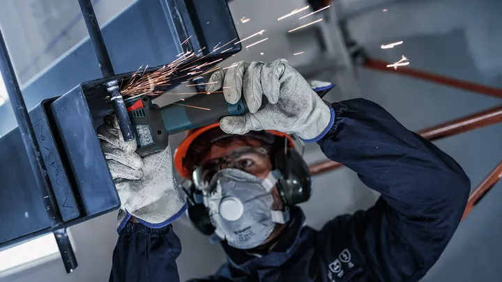 A person wearing safety equipment grinds metal, creating sparks.