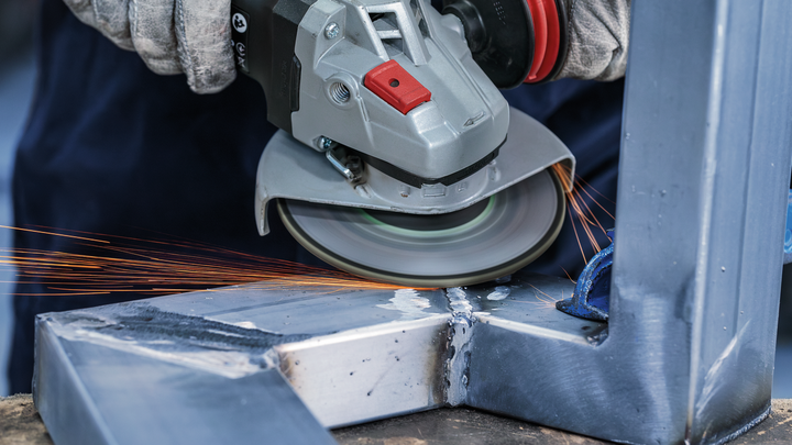 Person wearing safety equipment grinds a welded metal joint with an angle grinder.