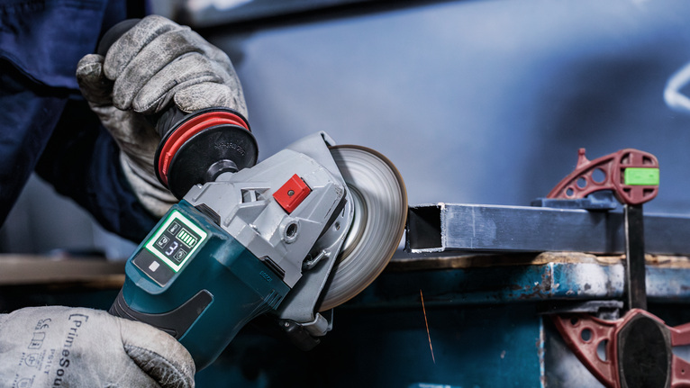 Person wearing safety equipment grinds metal with an angle grinder.