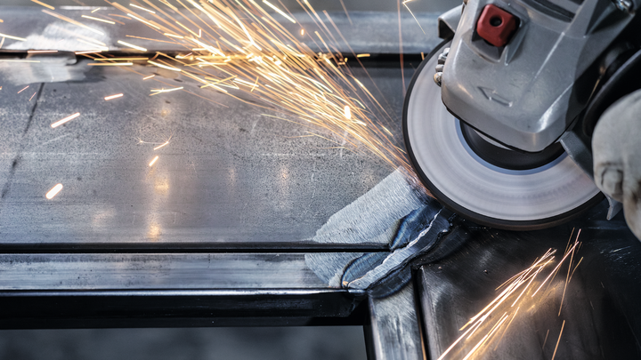Person wearing safety equipment grinds metal, producing bright sparks.