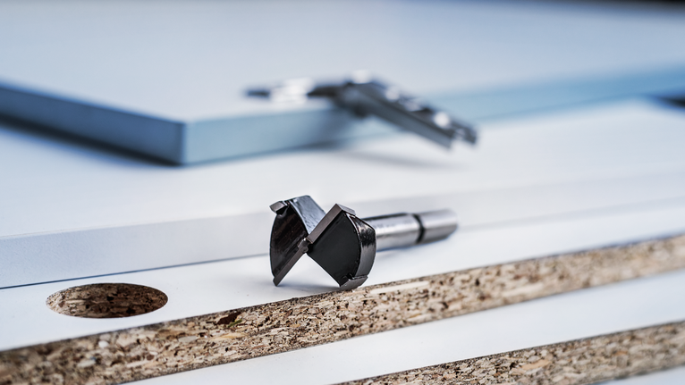 Drill bit and caliper placed on stacked laminated boards with a drilled hole.