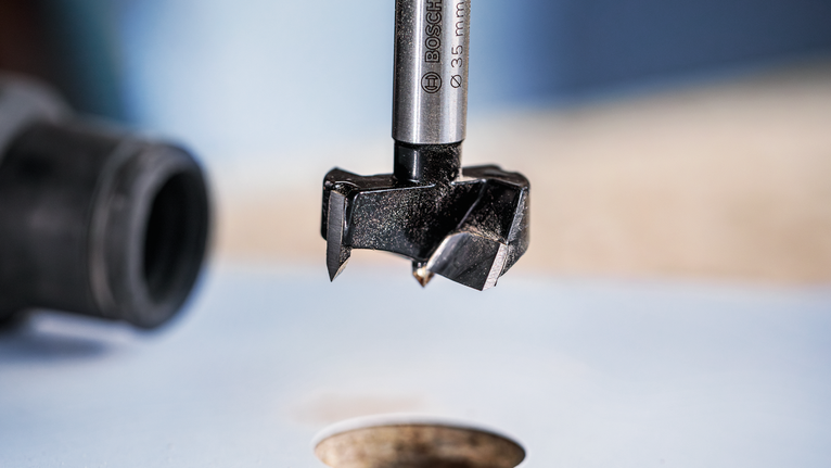 Forstner drill bit positioned above a freshly drilled hole in wood.