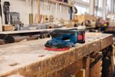 Cordless random orbit sander resting on a worn wooden workbench in a workshop.