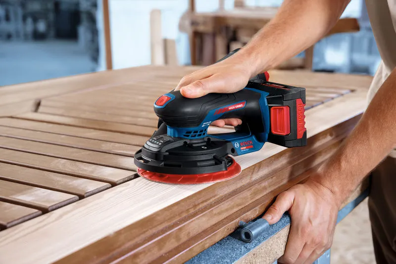 A person sands a wooden door using a cordless random orbit sander.