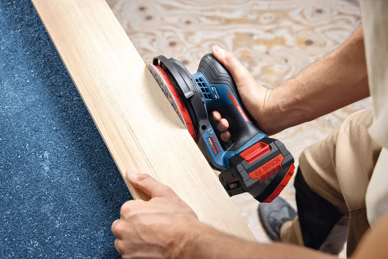 A person sands a wooden plank using a cordless random orbit sander.