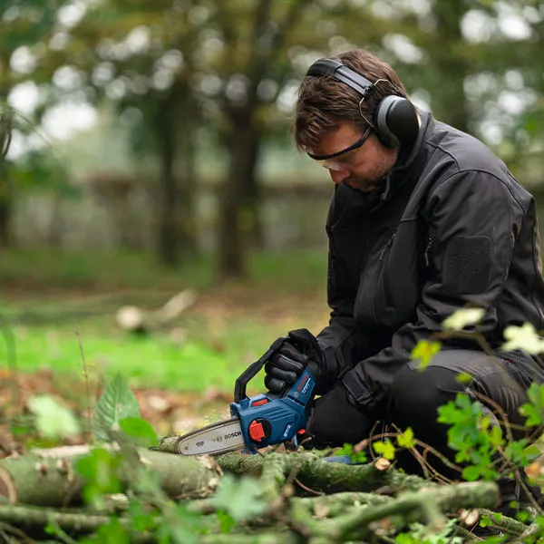 A person wearing safety equipment trims tree branches with a cordless pruner saw.
