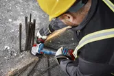 A person wearing safety equipment grinds rebar on a concrete surface with an angle grinder.