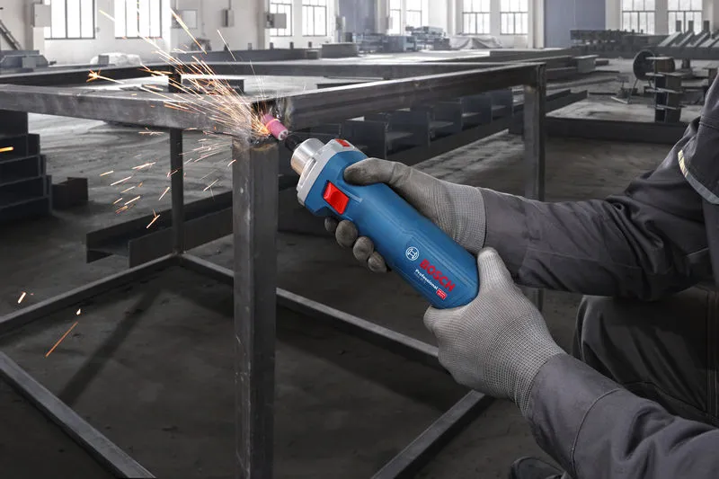 A person wearing safety equipment uses a straight grinder to smooth a metal frame.