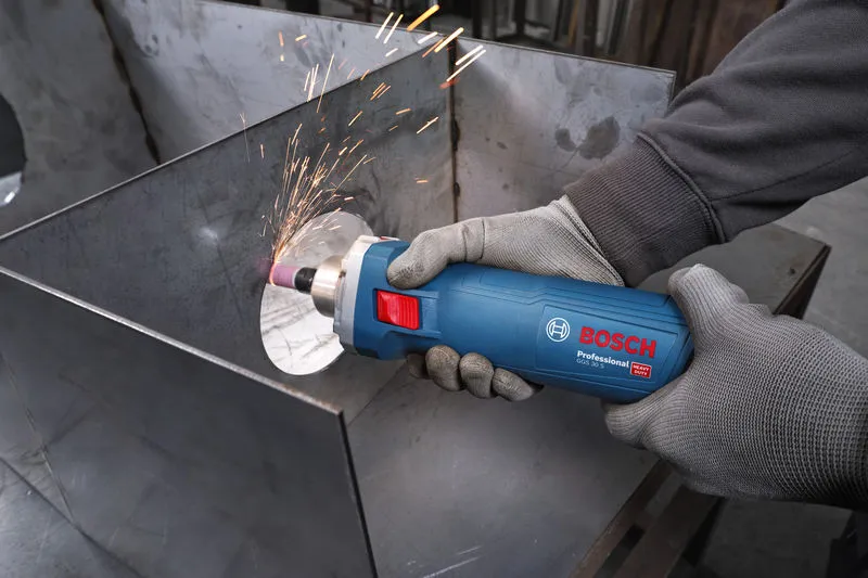 A person wearing safety equipment grinds metal with a straight grinder, creating sparks.