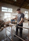 A person wearing safety equipment drills into a wooden frame in a workshop.