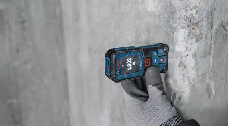 Person wearing safety equipment uses a laser measure against a concrete wall.