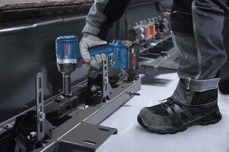 A person wearing safety equipment uses an impact wrench to fasten a bolt on a metal frame.