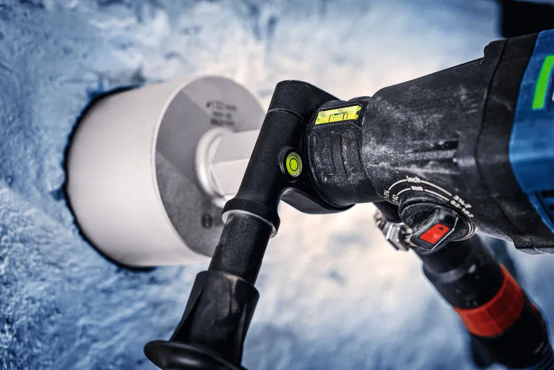 Diamond drill with a level attachment making a circular hole in a concrete wall.