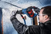 A person wearing safety equipment drills into a concrete wall with a diamond drill.