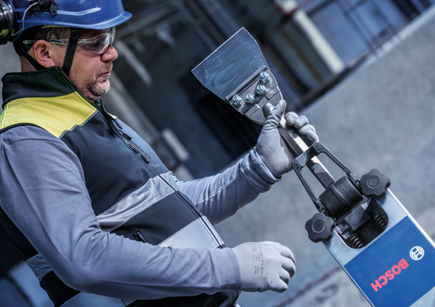 Person wearing safety equipment operates a heavy-duty scraper tool at a construction site.