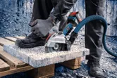 A person wearing safety equipment cuts a concrete slab with a cordless angle grinder.