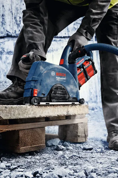 A person wearing safety equipment uses a cordless tool with dust extraction on a stone slab.