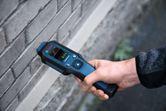 A person uses a material moisture meter to check moisture in a brick wall.