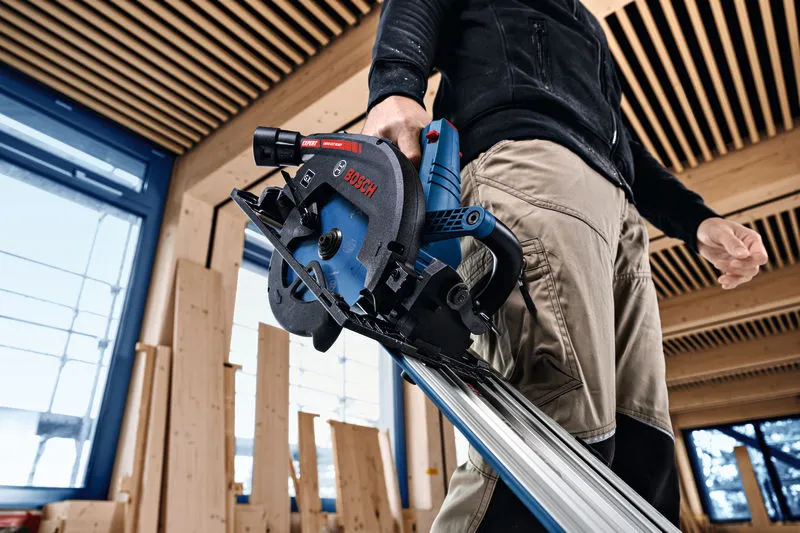 A person operates a cordless circular saw to cut a wooden board indoors.