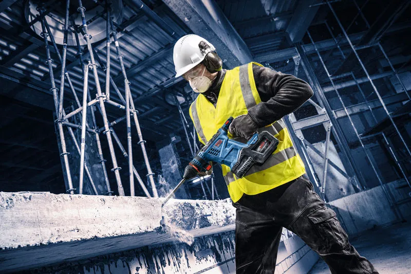 A person wearing safety equipment drills into concrete at a construction site.