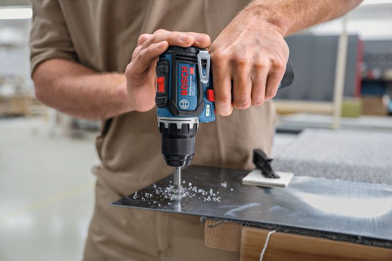 Person drills a hole in a metal sheet with a cordless power drill.