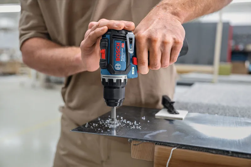 Person drills a hole in a metal sheet with a cordless power drill.