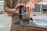 Person drills a hole in a metal sheet with a cordless power drill.