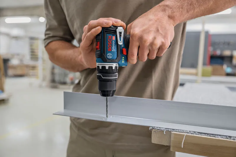 Person using a cordless drill to make a hole in a metal channel.