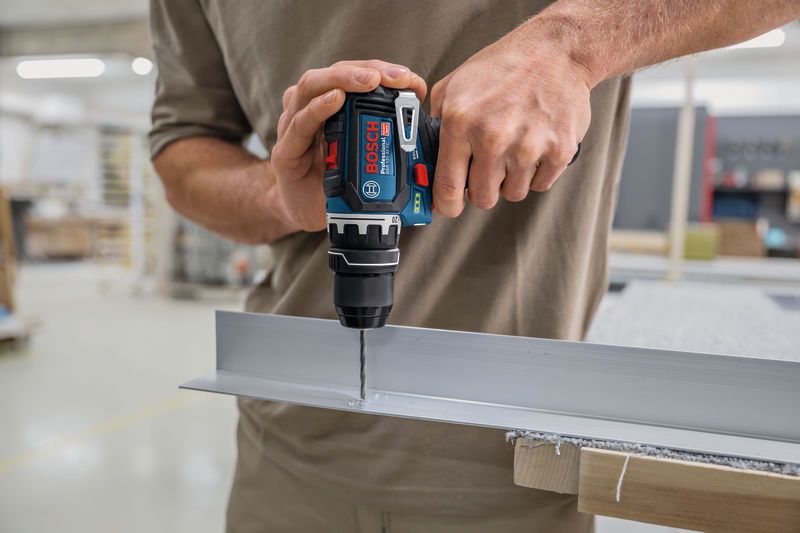 Person using a cordless drill to make a hole in a metal channel.