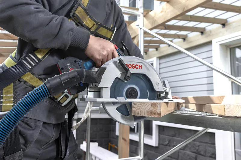 A person wearing safety equipment cuts wood with a cordless circular saw on scaffolding.