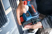 A person adjusts a cordless impact driver wearing safety equipment.