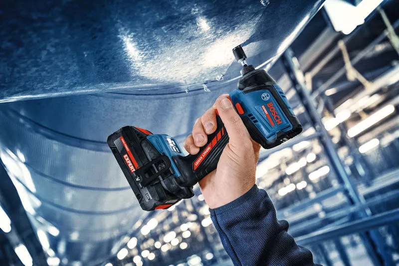 A person uses a cordless impact driver to fasten a bolt into metal overhead.