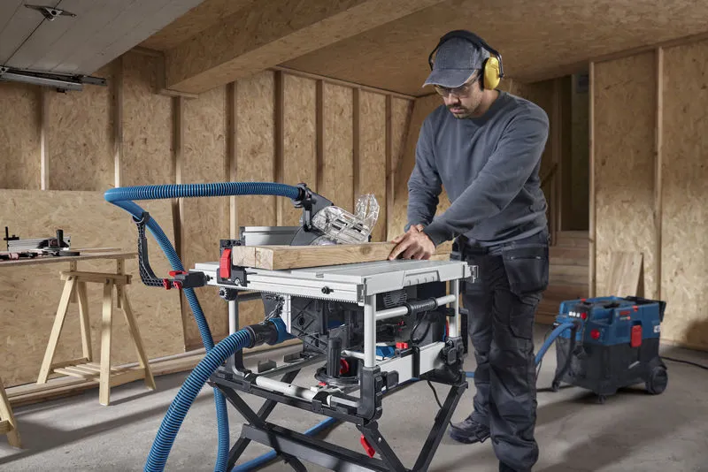 A person wearing safety equipment makes a wood cut using a table saw in a workshop.