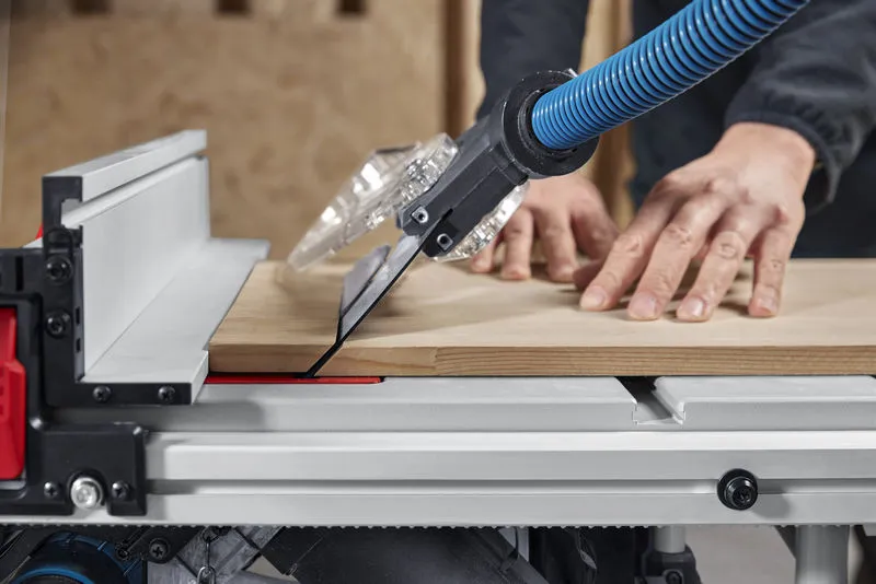 A person guides wood through a table saw with dust extraction mounted.