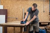 Person wearing safety equipment sanding a wooden cabinet door with a cordless random orbit sander.
