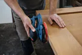 Person sanding a wooden board with a cordless random orbit sander.