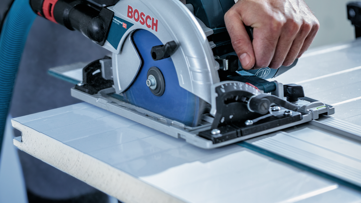 Person guides a circular saw along a metal rail to cut a panel.