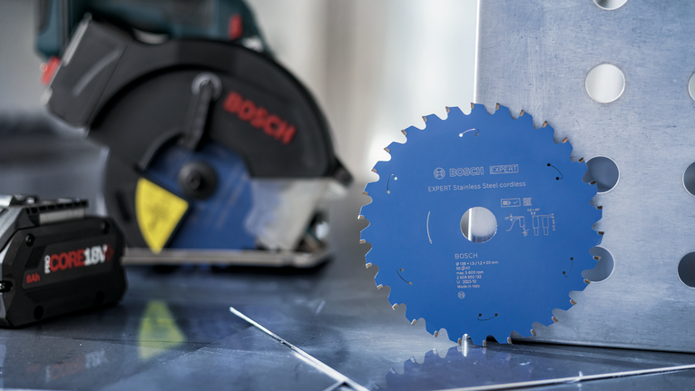 Circular saw blade displayed upright on a metal sheet beside a cordless power tool.