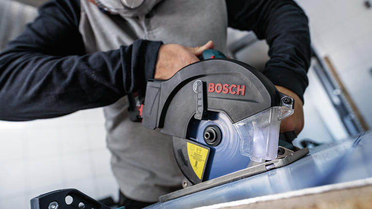Person wearing safety equipment cuts metal sheet with a circular saw.