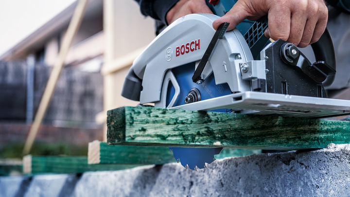 Person wearing safety equipment cuts green lumber with a circular saw.